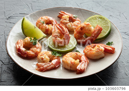 Shrimps. Cooked shrimp with lime on a white plate, on a black stone table 103603796