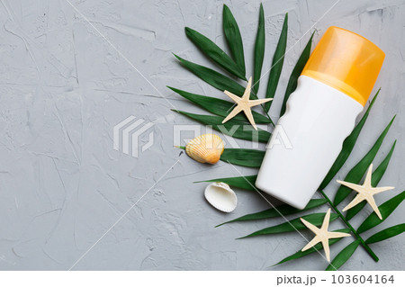 Sunscreen spray bottle. Bottle with sun protection cream and sea shells with tropical green leaf on color background, top view 103604164