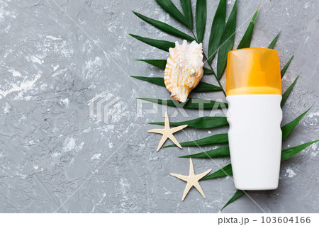 Sunscreen spray bottle. Bottle with sun protection cream and sea shells with tropical green leaf on color background, top view 103604166