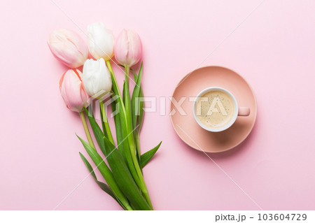 Spring background with flowers, a cup of coffee and a bouquet of pink and white tulips on colored table background with place for text. Copy space top view 103604729