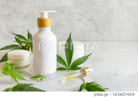 White One pump bottle near green cannabis leaves on white table. Cosmetic Mockup White One pump bottle near green cannabis leaves on white table. Cosmetic Mockup 103607004