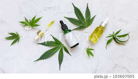 Cosmetic dropper bottles with blank label and pipette near green cannabis leaves. Mockup Cosmetic dropper bottles with blank label and pipette near green cannabis leaves. Mockup 103607005