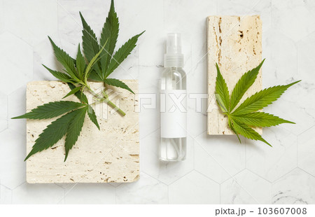Cosmetic Bottle with blank label near green cannabis leaves and beige stones top view. Mockup 103607008
