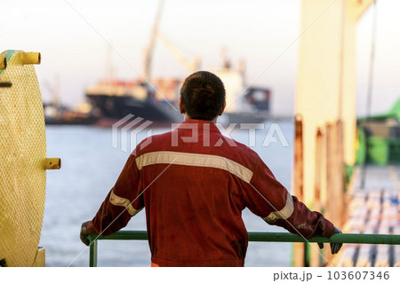 Seaman in red working overall and orange helmet on deck. Working at sea. Cargo vessel. Mooring operations. Able seaman. Seaman in red working overall and orange helmet on deck. Working at sea. Cargo vessel. Mooring operations. Able seaman. 103607346
