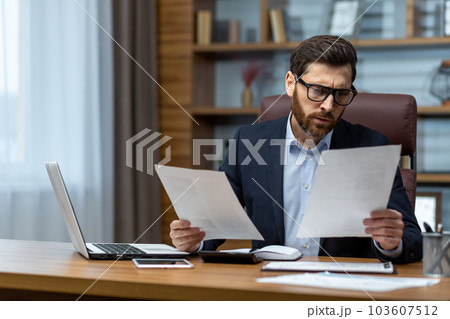 Serious and focused financier accountant on paper work inside office, mature man using calculator and laptop for calculating reports and summarizing accounts, businessman at work . 103607512