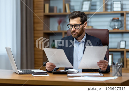 Serious and focused financier accountant on paper work inside office, mature man using calculator and laptop for calculating reports and summarizing accounts, businessman at work. 103607515
