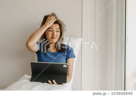 Woman works digital online on her bed feeling tired on vacation. Woman works digital online on her bed feeling tired on vacation. 103608840