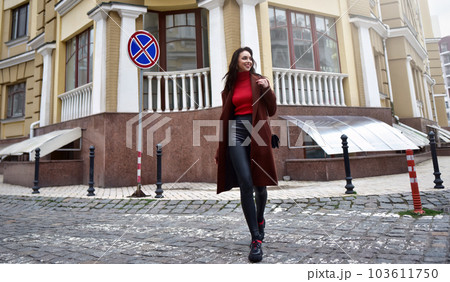 Beautiful woman with a purse on her shoulder in a brown coat is walking down the street. Beautiful woman with a purse on her shoulder in a brown coat is walking down the street. 103611750