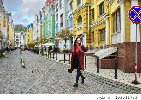Woman smiling runs across the road. A woman walks down the street with smile. Woman smiling runs across the road. A woman walks down the street with smile. 103611753