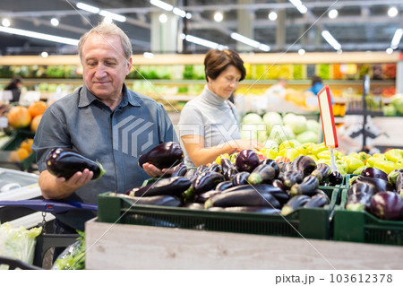 elderly man chooses eggplants in vegetable and fruit department 103612378