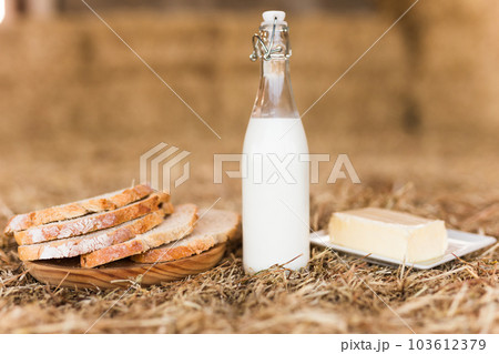 Milk bottle, slices of fresh wheat bread and butter on hay 103612379