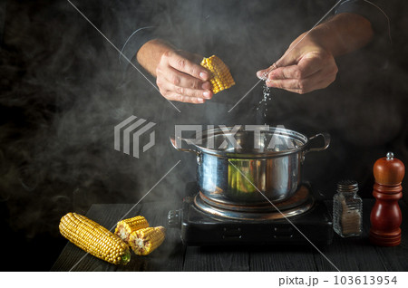 A professional chef adds salt to the pot when cooking corn. Work environment on a vintage kitchen table in a restaurant A professional chef adds salt to the pot when cooking corn. Work environment on a vintage kitchen table in a restaurant 103613954