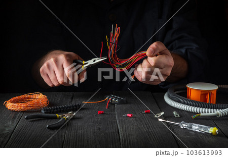 Electrical wires for connecting. Repair of electrical equipment in the workshop of a master electrician. Close-up of the hands of professional master during work. 103613993