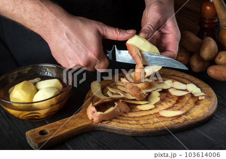 Professional chef peels potatoes for French fries. For potato dishes. On black background concept for menu, cooking, healthy food. Free advertising space Professional chef peels potatoes for French fries. For potato dishes. On black background concept for menu, cooking, healthy food. Free advertising space 103614006