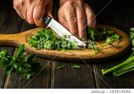 Cutting green parsley on a cutting board with a knife for cooking vegetarian food. Peasant food 103614098