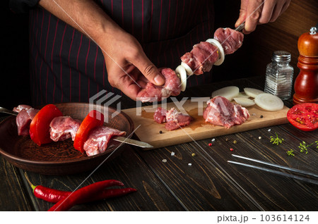 The process of cooking meat kebab in the restaurant kitchen. The chef spears raw lamb meat on a skewer with onions 103614124