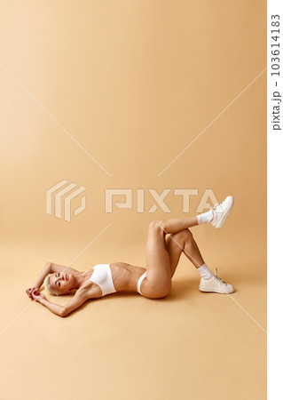 Tender, attractive young girl with blonde short hair, lying on floor in underwear and sneakers against pastel yellow studio background Tender, attractive young girl with blonde short hair, lying on floor in underwear and sneakers against pastel yellow studio background 103614183