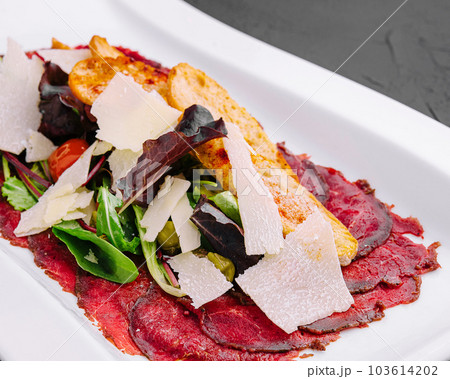Beef carpaccio with salad and Parmesan on a white plate 103614202