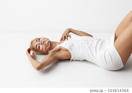Portrait of attractive blonde woman, beautiful model posing in white singlet, homewear against grey studio background Portrait of attractive blonde woman, beautiful model posing in white singlet, homewear against grey studio background 103614368