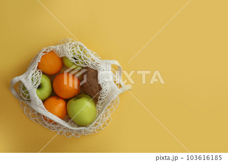 Net bag with fruits on yellow background, top view. Space for text Net bag with fruits on yellow background, top view. Space for text 103616185