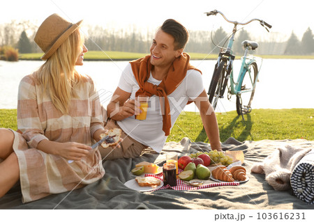 Happy young couple having picnic near lake on sunny day 103616231