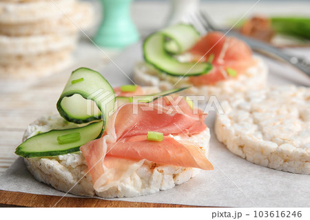 Puffed rice cakes with prosciutto and cucumber on wooden board, closeup 103616246