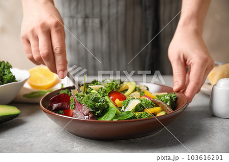 Woman cooking tasty kale salad on light grey table, closeup Woman cooking tasty kale salad on light grey table, closeup 103616291