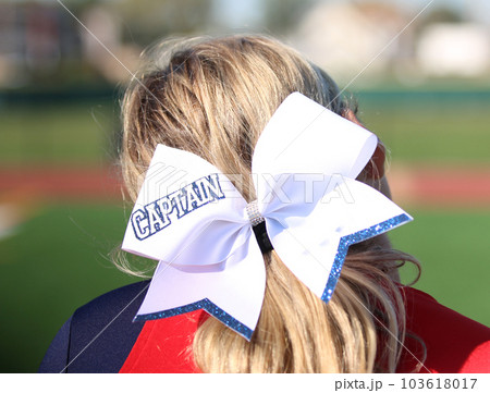 Cheerleader wearing a large white bow with captain written on it 103618017