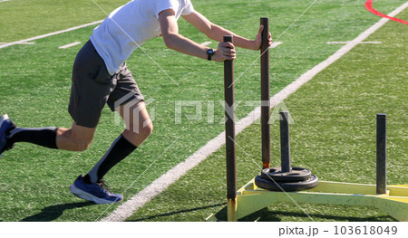 Runner pushing a sled with weights on a turf field 103618049