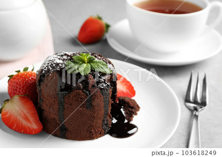 Delicious warm chocolate lava cake with mint and strawberries on table, closeup 103618249