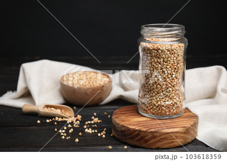 Jar with green buckwheat on black wooden table. Space for text Jar with green buckwheat on black wooden table. Space for text 103618359