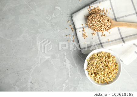 Bowl of sprouted green buckwheat and spoon with grains on light grey table, flat lay. Space for text 103618368