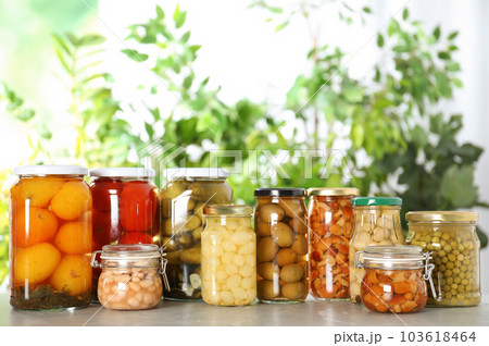 Glass jars of different pickled vegetables on marble table 103618464