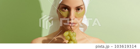 Woman using grapeseed-based eye patches on pastel green background. Natural sustainable skincare 103619314