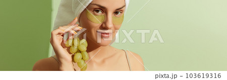 Woman using grapeseed-based eye patches on pastel green background. Natural sustainable skincare Woman using grapeseed-based eye patches on pastel green background. Natural sustainable skincare 103619316