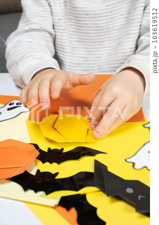 A child creates a pumpkin out of paper. Origami for Halloween, preparation A child creates a pumpkin out of paper. Origami for Halloween, preparation 103619512