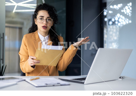 Portrait of disappointed business woman, latin american received notification letter from bank with bad news, office worker looking sad at camera, working at work using laptop. 103622320