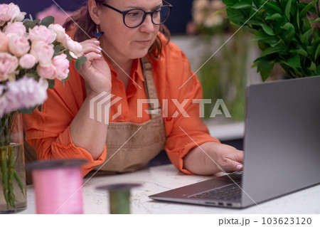 florist and business owner in the flower shop accepts orders using laptop and expertly creates arrangements, ready for pick-up or delivery. 103623120
