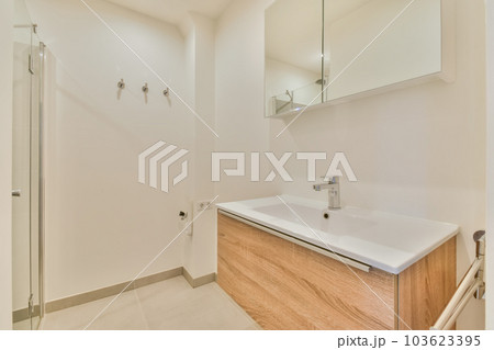 a bathroom with white walls and wood cabinetd vanity in the middle part of the room there is a mirror on the wall 103623395