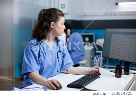 Caucasian nurse checking appointments list on computer monitor, sitting at clinic desk. Focused adult woman healthcare expert working in medical office with stethoscope around neck 103624826