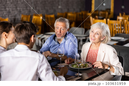 Young family and elderly couple of spouses eating in cafe celebrating event and communicating 103631959