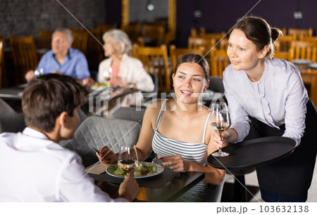 Waitress serving drinks to young couple sitting at table in restaurant 103632138