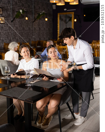 Young male waiter taking order from two women in restaurant 103632155