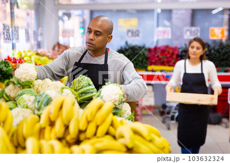 Supermarket employee lays out cauliflower on shelves 103632324