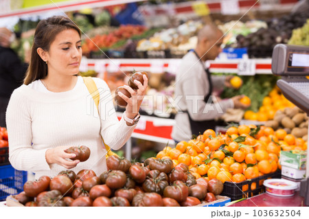 Satisfied female customer choosing fresh black tomatoes in shop 103632504