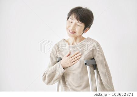 松葉杖を持って胸を撫で下ろす中年女性 白背景 松葉杖を持って胸を撫で下ろす中年女性 白背景 103632871