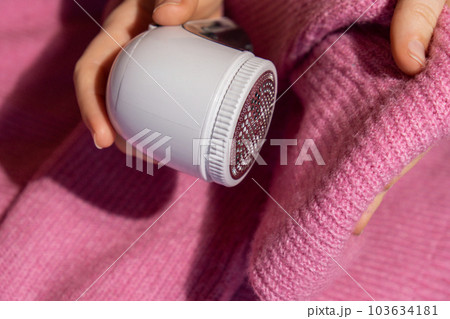 Woman using Anti-pilling razor at home. Device for shaving clothes. Anti-Plush fabric Shaver. Electric portable sweater pill defuzzer Lint remover from pink acrylic or wool sweater. Slow fashion Woman using Anti-pilling razor at home. Device for shaving clothes. Anti-Plush fabric Shaver. Electric portable sweater pill defuzzer Lint remover from pink acrylic or wool sweater. Slow fashion 103634181