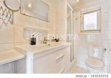 a modern bathroom with white tiles and marble flooring, along with a large mirror on the wall above the sink 103638358