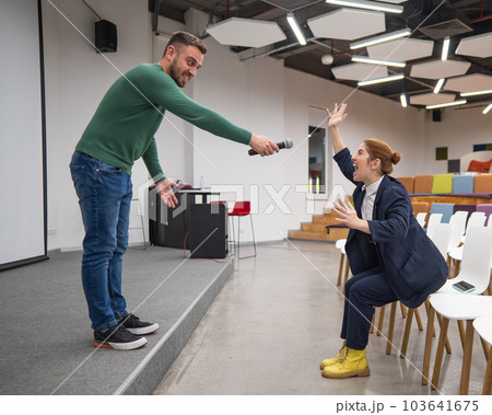 A red-haired Caucasian business woman sits in the front row in an empty conference room. Bearded man asks a question in the hall. A red-haired Caucasian business woman sits in the front row in an empty conference room. Bearded man asks a question in the hall. 103641675