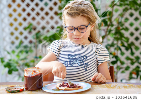 Cute funny preschool girl eats sweet bun for breakfast. Happy child eating bread roll with strawberry, cherry or plum jam. Health food for children and kids with selfmade jelly Cute funny preschool girl eats sweet bun for breakfast. Happy child eating bread roll with strawberry, cherry or plum jam. Health food for children and kids with selfmade jelly 103641688